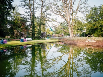 Staatsbad Salzuflen - Kurparksee Kurparksee in Bad Salzuflen mit klarer Wasseroberfläche, die üppige Bäume und Sitzgelegenheiten spiegelt.