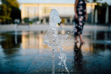 Konzerthallenvorplatz Ein Springbrunnen spritzt Wasser in die Luft, im Hintergrund ist ein unscharfer Gebäudeeingang zu sehen.