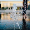 Konzerthallenvorplatz Ein Springbrunnen spritzt Wasser in die Luft, im Hintergrund ist ein unscharfer Gebäudeeingang zu sehen.