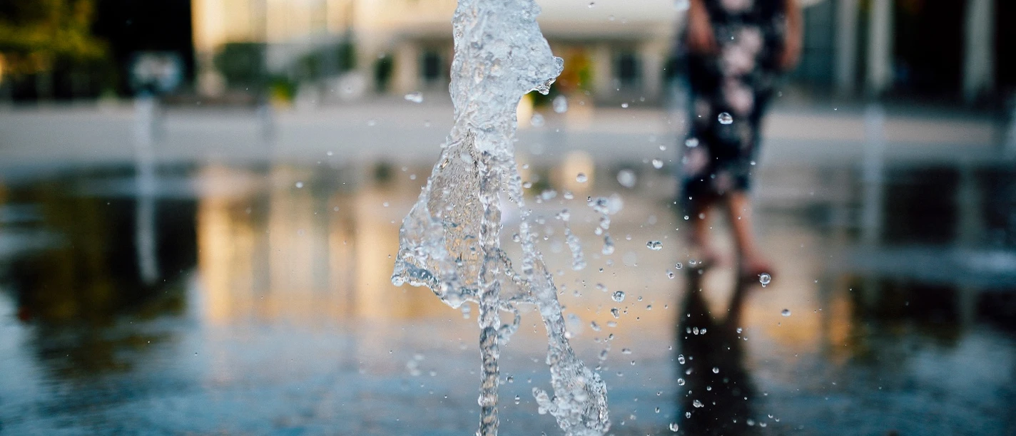 Konzerthallenvorplatz Ein Springbrunnen spritzt Wasser in die Luft, im Hintergrund ist ein unscharfer Gebäudeeingang zu sehen.