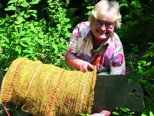 Sigrid Schröder Sigrid Schröder präsentiert eine große, goldene Skulptur inmitten üppiger, sommerlich grüner Natur.