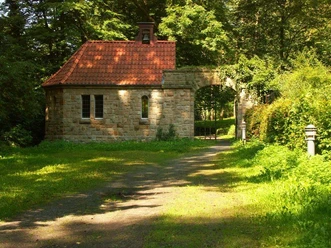 Friedhofskapelle Lengerich Steinerne Friedhofskapelle mit rotem Ziegeldach, umgeben von Bäumen und einem Weg im Grünen.