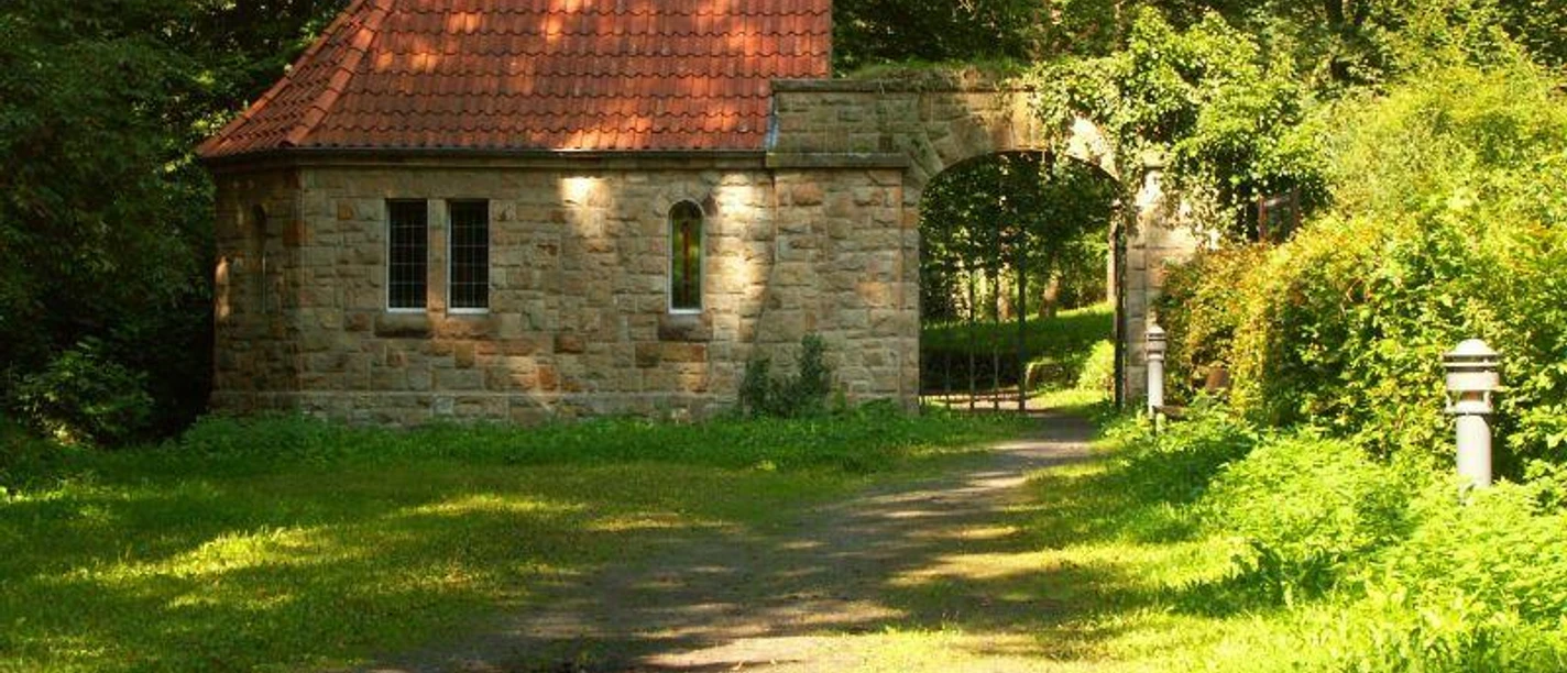 Friedhofskapelle Lengerich Steinerne Friedhofskapelle mit rotem Ziegeldach, umgeben von Bäumen und einem Weg im Grünen.