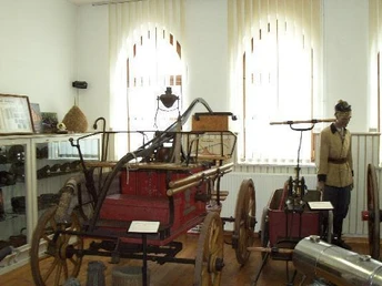 Feuerwehrmuseum Schröttinghausen Historische Feuerwehruniformen und -geräte, darunter eine antike Handdruckspritze, im Museum ausgestellt.