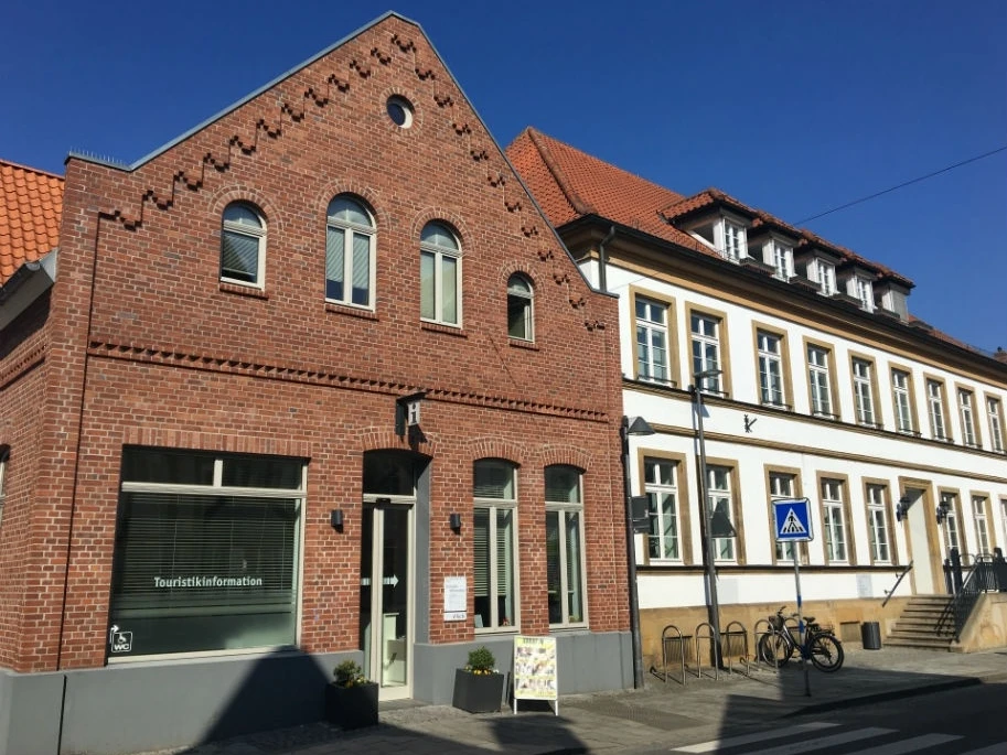 Backstein-Touristikinformation und angrenzendes Gebäude bei sonnigem Wetter; blaue Straßenbeschilderung.