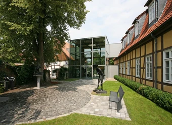 Moderne Glasfassade verbindet historische Fachwerkgebäude in gepflegter Parklandschaft.