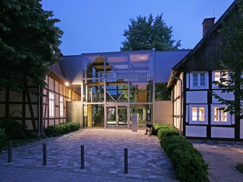 Kunsthaus bei Dämmerung Moderne gläserne Eingangshalle verbindet historische Fachwerkgebäude mit beleuchtetem Innenhof.