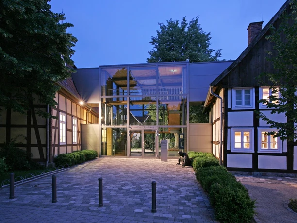 Kunsthaus bei Dämmerung Moderne gläserne Eingangshalle verbindet historische Fachwerkgebäude mit beleuchtetem Innenhof.