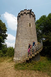 Holsterturm Historischer Holsterturm aus Stein mit Zinnen, umgeben von Bäumen. Zwei Menschen auf der Wendeltreppe.