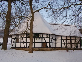 Rossmühle Oberbauerschaft Historische Fachwerkscheune mit schneebedecktem Dach, umgeben von kahlen Bäumen im Winter.