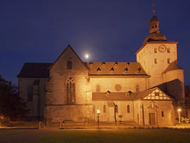 Eggeedom Neuenheerse Neuenheerse: Historische Steinkirche bei Nacht, angestrahlt, mit Uhrturm und beleuchteten Fenstern.
