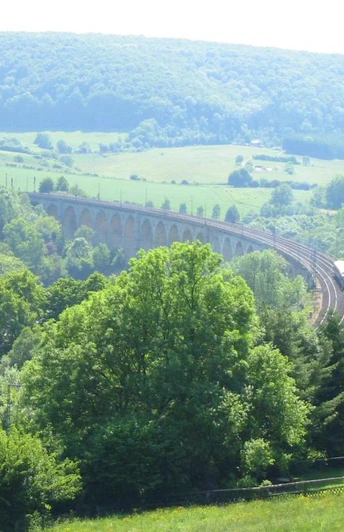 Blick auf den Viadukt Graues Viadukt schlängelt sich durch grüne bewaldete Hügellandschaft unter blauem Himmel.