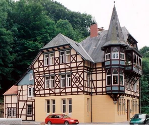 Neuer Krug Historisches Fachwerkhaus mit drei Stockwerken und einem markanten spitzen Turm in bewaldeter Umgebung.
