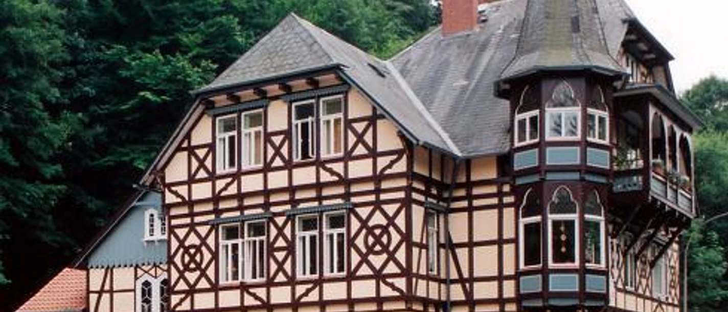 Neuer Krug Historisches Fachwerkhaus mit drei Stockwerken und einem markanten spitzen Turm in bewaldeter Umgebung.