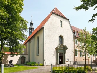 Eine helle Kirche mit rotem Dach, flankiert von Bäumen und einem angrenzenden Glockenturm.