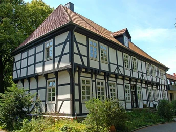 Das Herrenhaus in Stift Quernheim aus Fachwerk steht inmitten einer grünen Umgebung neben Bäumen.