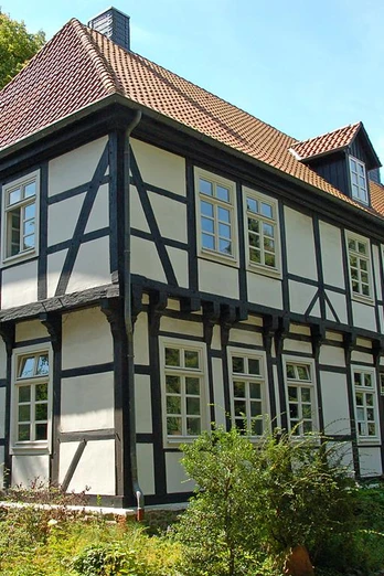 Herrenhaus in Stift Quernheim Das Herrenhaus in Stift Quernheim aus Fachwerk steht inmitten einer grünen Umgebung neben Bäumen.
