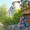 Ein Paar sitzt auf einer Steinmauer vor der historischen Levedags Mühle, umgeben von grüner Natur.