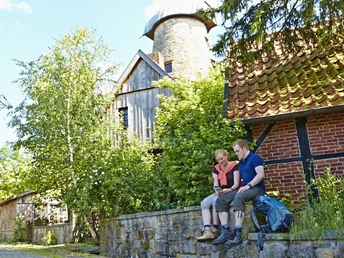 Ein Paar sitzt auf einer Steinmauer vor der historischen Levedags Mühle, umgeben von grüner Natur.