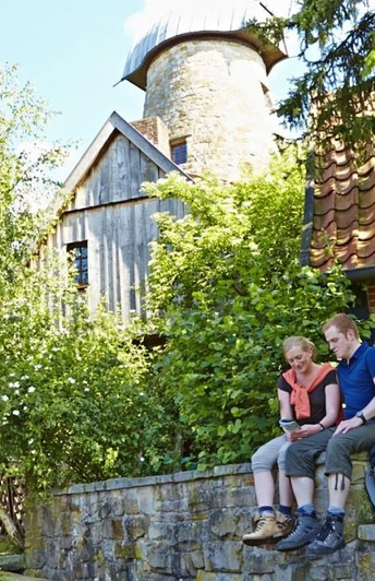Ein Paar sitzt auf einer Steinmauer vor der historischen Levedags Mühle, umgeben von grüner Natur.