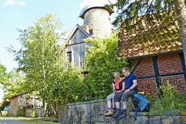 Levedags Mühle: Rast Ein Paar sitzt auf einer Steinmauer vor der historischen Levedags Mühle, umgeben von grüner Natur.