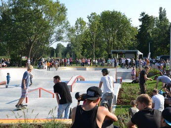 Menschen unterschiedlicher Altersgruppen genießen einen sonnigen Tag im Skatepark mit Grünflächen und Bäumen.
