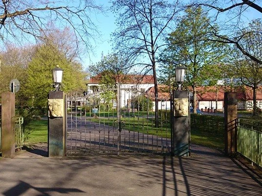 Schützenplatz Paderborn - Löwentor Eingang mit Löwentor zum Schützenplatz Paderborn, umgeben von Bäumen und blauer Himmel im Hintergrund.