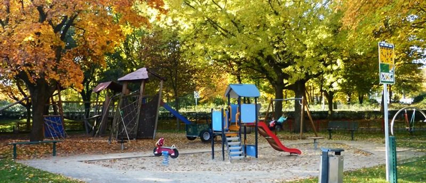 Spielplatz am Maspernplatz mit Rutsche, Klettergerüst, Wipptier, umgeben von herbstlichen Bäumen.