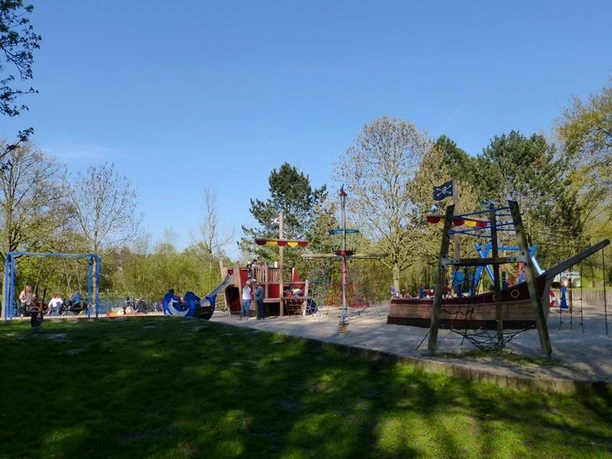 Spielplatz am Padersee Abenteuerspielplatz am Padersee mit Piratenschiff, Klettergeräten und Schaukeln, umgeben von Bäumen.