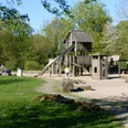 Spielplatz in der Paderaue Spielplatz mit Holzklettergerüst und Rutsche, umgeben von grünen Bäumen und Wiese.