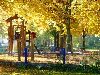 Spielplatz im Riemekepark Im Riemekepark lädt ein Spielplatz mit Klettergerüst und Rutsche, umgeben von herbstlichen Bäumen, ein.