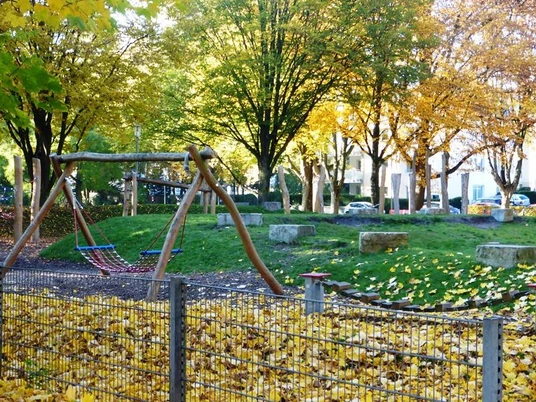 Spielplatz im Riemekepark Spielplatz im Riemekepark mit Holzschaukeln, Klettergerüst und buntem Herbstlaub unter Bäumen.