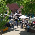 Mardorfer Kunsthandwerkermarkt Besucher schlendern durch einen sonnigen Kunsthandwerkermarkt, umgeben von Bäumen und historischem Backstein.