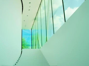 Moderne Treppe mit weißen Stufen, flankiert von einer hohen Glaswand, an einem klaren Tag.