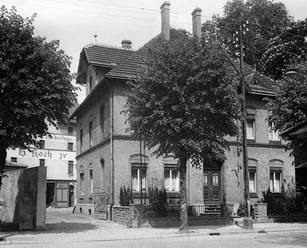 Historische Villa mit Backsteinmauerwerk, Flügeltüren und markanten Fenstern, umgeben von Bäumen.
