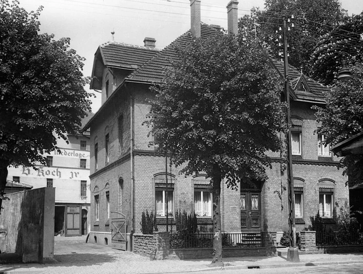 Historische Villa mit Backsteinmauerwerk, Flügeltüren und markanten Fenstern, umgeben von Bäumen.