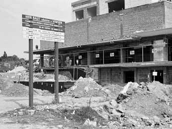 Eine Baustelle für ein Einkaufszentrum mit unfertigem Gebäude und einem großen Bauschild im Vordergrund.
