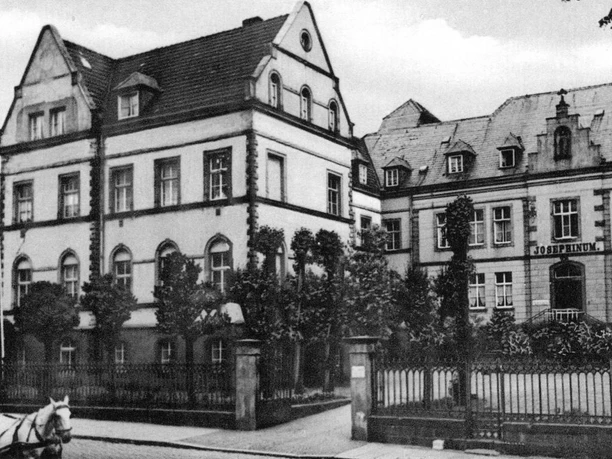 Schwarzweiß-Foto von zwei historischen Gebäuden nebeneinander; rechts ein Schild mit "Josephinum".