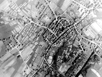 Ein Luftbild einer Siedlung, umgeben von landwirtschaftlichen Flächen und durchzogen von Straßen.