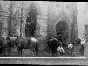 Historische Schwarzweißaufnahme einer teils zerstörten Synagoge mit davorstehenden Pferden, 1941.