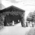 Historisches Foto eines Pavillons mit Rankpflanzen, umgeben von Frauen in Kleidung des 19. Jahrhunderts.