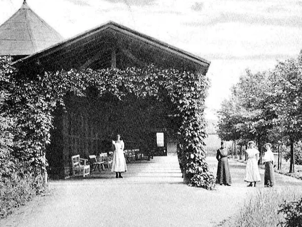 Caspar-Heinrich-Quelle Historisches Foto eines Pavillons mit Rankpflanzen, umgeben von Frauen in Kleidung des 19. Jahrhunderts.