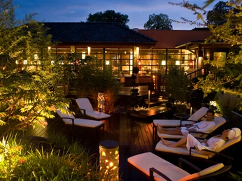 Sauna-Außenbereich am Abend Ein beleuchteter Sauna-Außenbereich in der Dämmerung, umgeben von Pflanzen, mit Liegen für Entspannung.