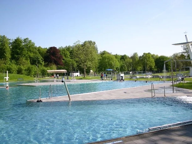 Ein modernes Freibad mit mehreren Schwimmbecken, grüner Umgebung und einem markanten Sprungturm.