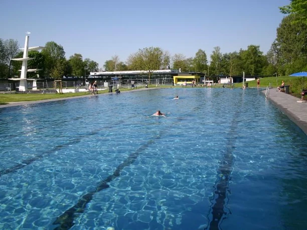 Schwimmer im Freibad schwimmen in einem großen, langen Becken unter blauem Himmel und umgeben von Bäumen.