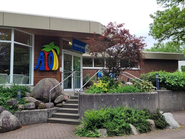 Eingangsbereich des Atoll-Freizeitbads mit Treppenstufen, umliegender Vegetation und buntem Logo.