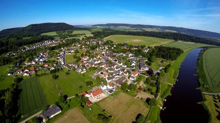 Wehrden zwischen Weser und Wildberg Luftaufnahme von Wehrden, umgeben von Wiesen und Wäldern, mit der Weser rechts im Bild.