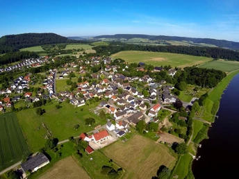 Wehrden zwischen Weser und Wildberg Luftaufnahme von Wehrden, umgeben von Wiesen und Wäldern, mit der Weser rechts im Bild.