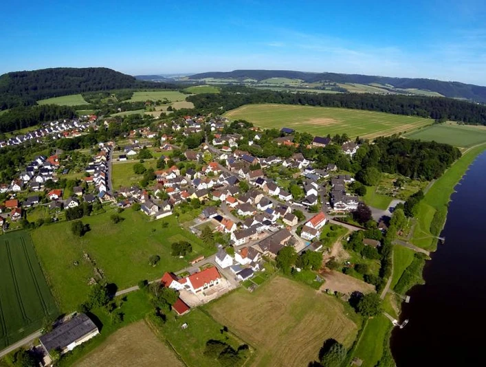 Wehrden zwischen Weser und Wildberg Luftaufnahme von Wehrden, umgeben von Wiesen und Wäldern, mit der Weser rechts im Bild.