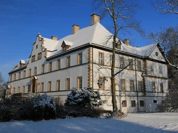 im Schlosspark Wehrden Schnee bedecktes Schloss umgeben von Bäumen unter klarem blauen Himmel im Schlosspark Wehrden.